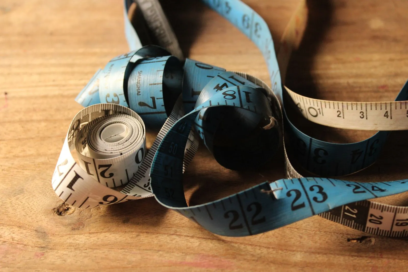 Rolled measuring tape on wooden surface, showing numbers for sewing or tailoring.